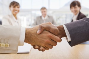 Portrait of happy businesspeople shaking hands together with colleges in background